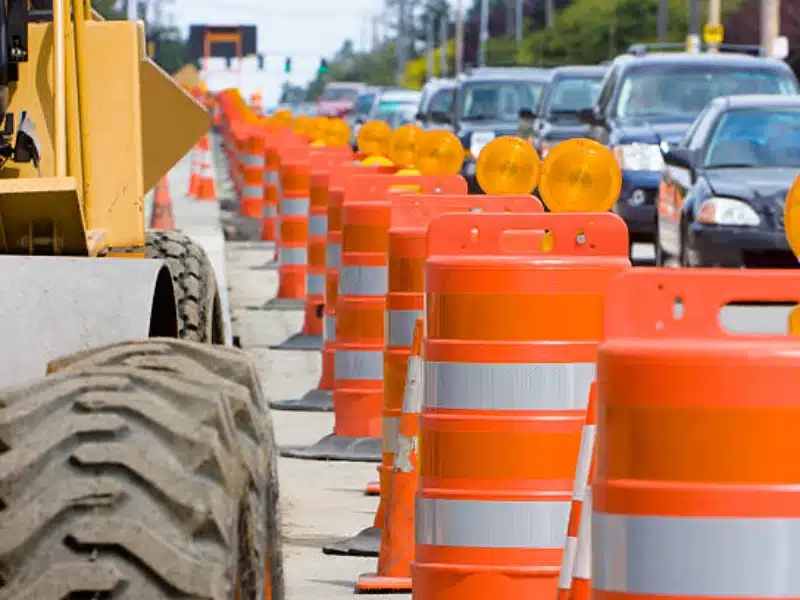 Highway construction zone with orange traffic barrels and warning lights guiding vehicles through work area.