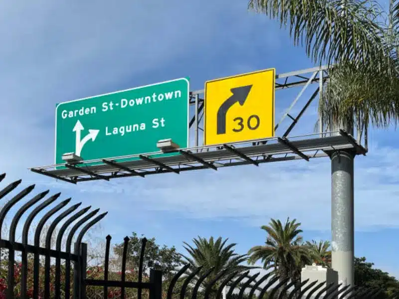 Freeway overhead signage with directional guide sign and yellow curve warning sign showing 30 mph speed limit.