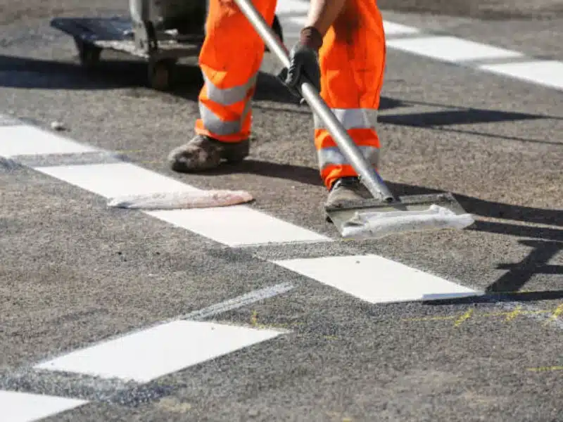 Road marking crew painting crosswalk stripes on asphalt with hand tools during pavement striping project